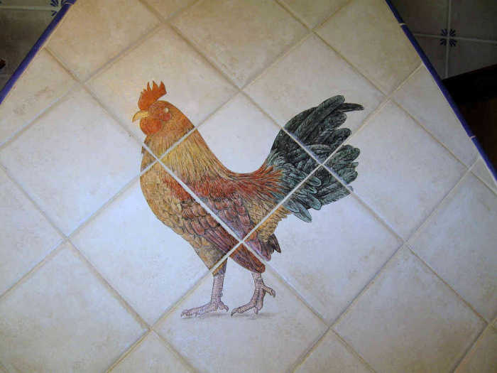 European Style Country Kitchen. Closeup of a proud rooster that adorns the tile stove hood vent and overlooks the kitchen. Painted by Julia Sweda.