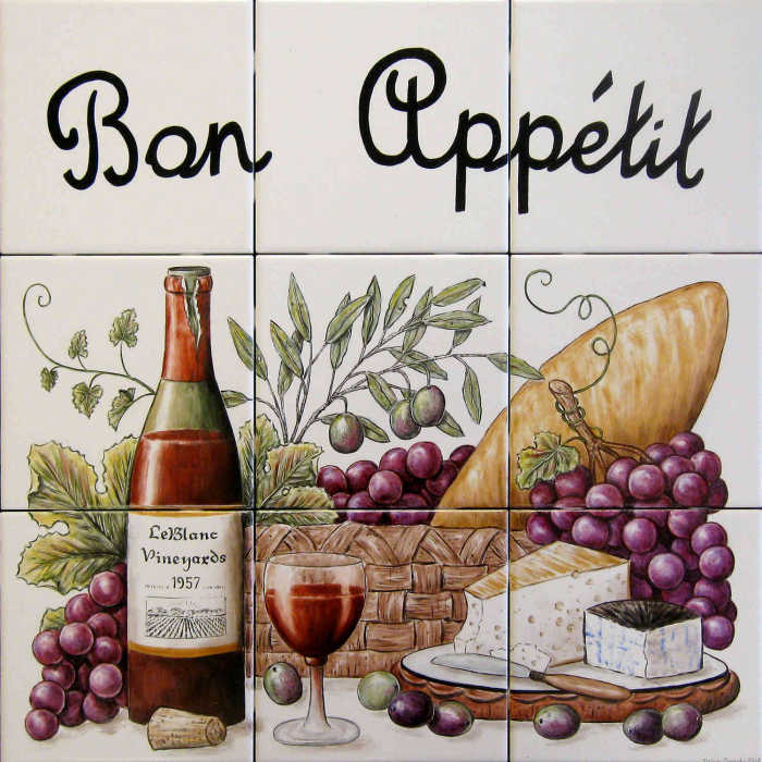Features baguette bread, two cheeses, basket of red grapes, olives and bottle of wine.