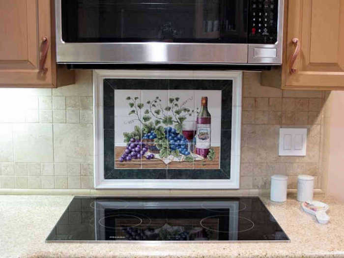 Spaich Vineyards Grapes Wine Art Old World Style Still Life, the backsplash tile mural installed behind cooktop with black and white border tiles. Artist Julia Sweda.
